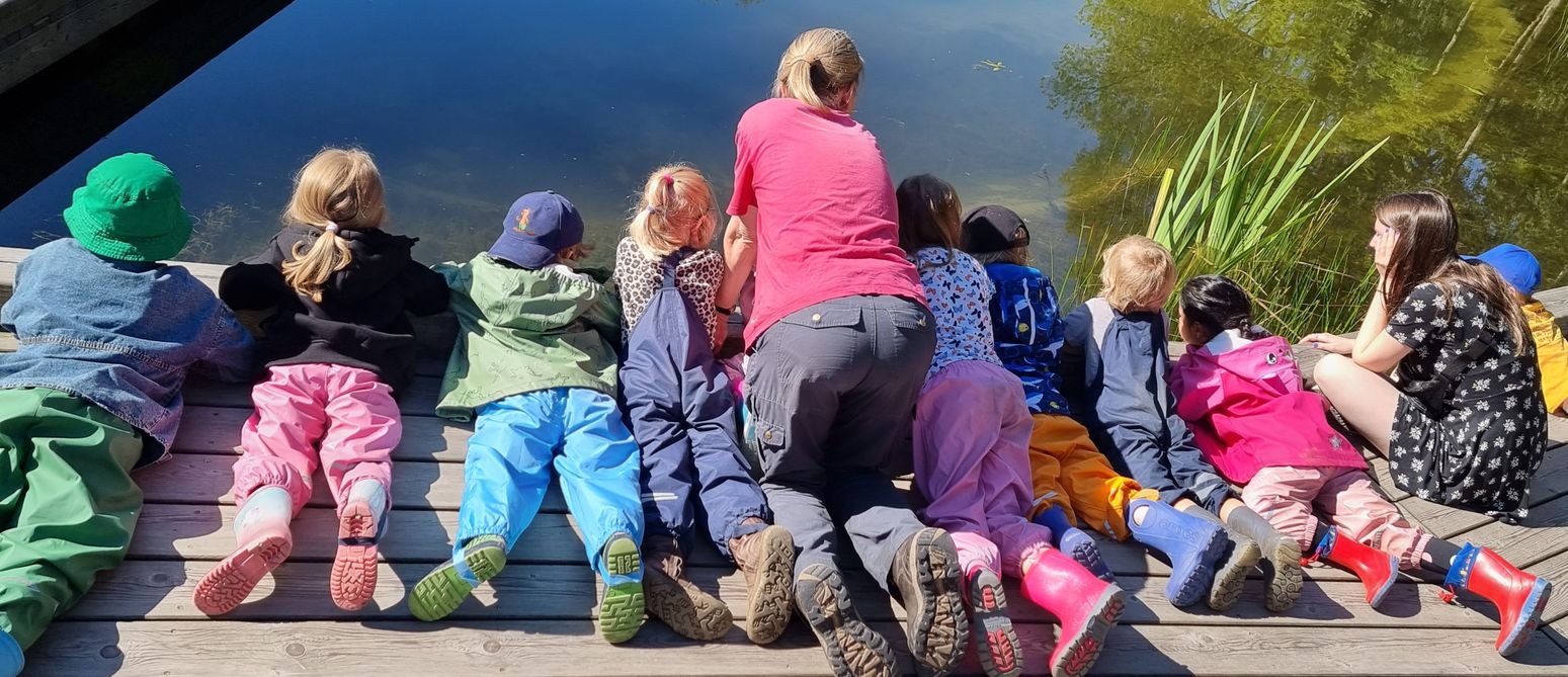 Zwei Erzieherinnen schauen sich zusammen mit den Kindern einen Teich genauer an